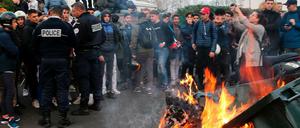 Polizisten sprechen neben einer brennenden Mülltonne mit protestierenden Schülern.