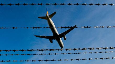 Ein Flugzeug fliegt über Stacheldraht hinweg. (Symbolbild)