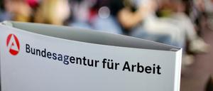 Ein Schild mit der Aufschrift "Bundesagentur für Arbeit" steht einem vollen Wartezimmer im Jobcenter. 