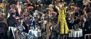 Mimi (Nadja Mchantaf) und Marcello (Günter Papendell) sitzen am Tisch, während Musetta (Vera-Lotte Böcker) tanzt. 