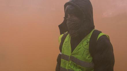 Ein vermummter Demonstrant der sogenannten "Gelbwesten" steht in dichtem Rauch von Rauchgranaten. 
