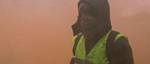Ein vermummter Demonstrant der sogenannten "Gelbwesten" steht in dichtem Rauch von Rauchgranaten. 