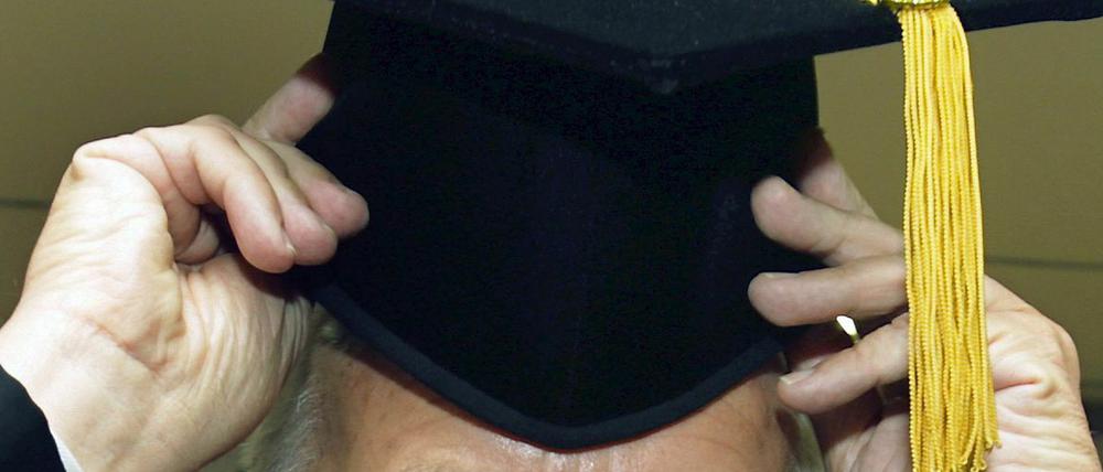 Ein Doktorand setzt sich bei der Titelverleihung den Doktorhut auf. 