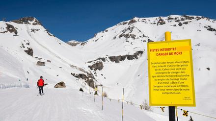 Ein Skifahrer fährt an einem Warnschild vorbei, welches nahe an der Stelle steht, an welcher eine Lawine abgegangen ist.