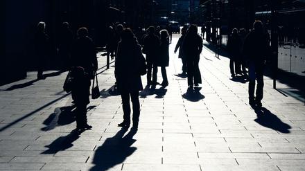 Im Gegenlicht zeichnen sich Passanten auf einem Gehweg als dunkle Silhouetten ab.