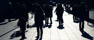 Im Gegenlicht zeichnen sich Passanten auf einem Gehweg als dunkle Silhouetten ab.
