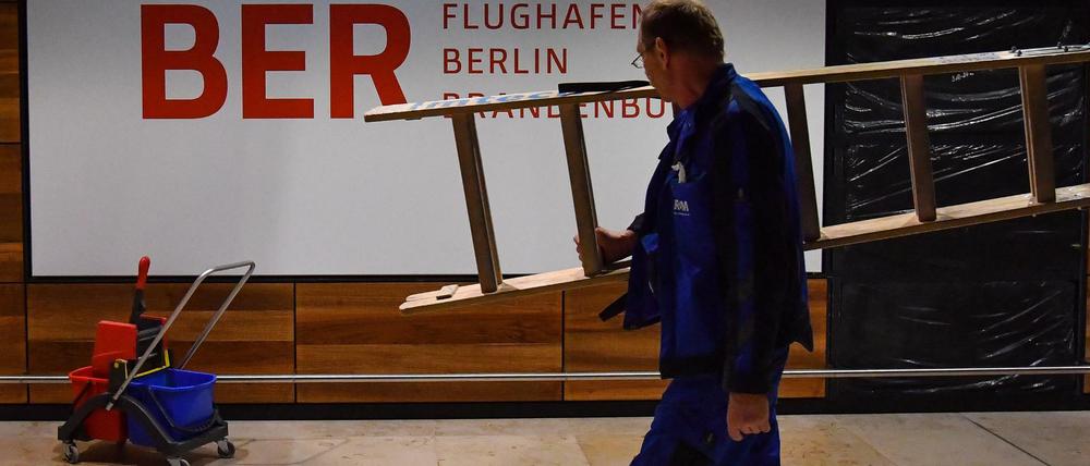 Arbeiter mit Leiter vor Flughafen-BER-Schild.