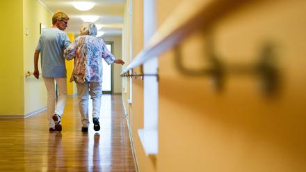 Eine Pflegekraft geht in einem Pflegeheim mit einer älteren Dame über einen Korridor. 