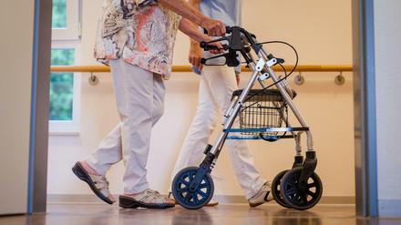 Eine Pflegekraft geht in einem Pflegeheim mit einer älteren Dame über einen Korridor. 