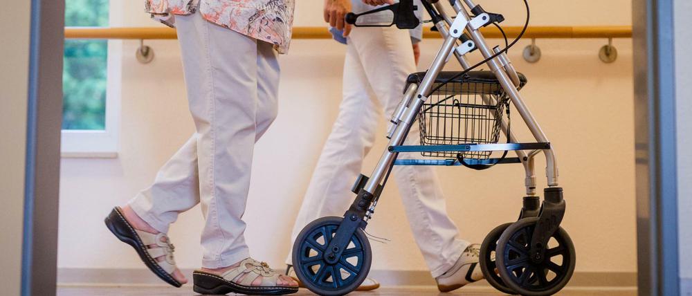 Eine Pflegekraft geht in einem Pflegeheim mit einer älteren Dame über einen Korridor. 
