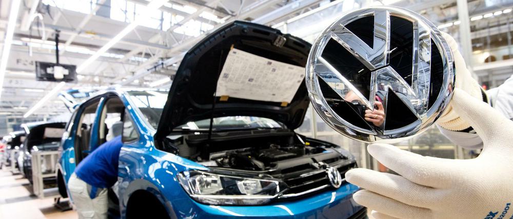 Ein VW-Mitarbeiter zeigt das Markenlogo kurz vor Einbau in einen Volkswagen Touran in der Endmontage im VW Werk. (Archivbild 2019)