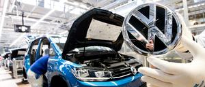 Ein VW-Mitarbeiter zeigt das Markenlogo kurz vor Einbau in einen Volkswagen Touran in der Endmontage im VW Werk. (Archivbild 2019)