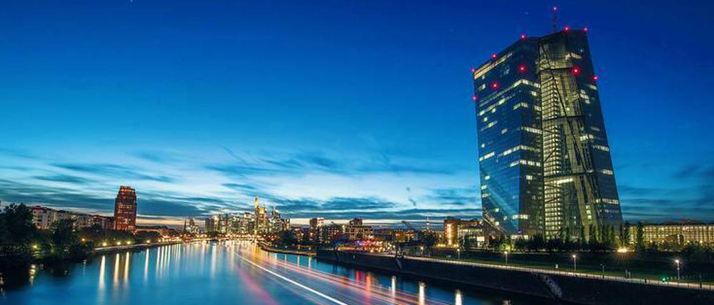 Die Europäische Zentralbank in Frankfurt am Main leuchtet in der Abenddämmerung, während ein vorbeifahrendes Schiff Lichtspuren zieht. 