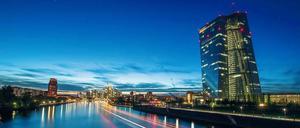 Die Europäische Zentralbank in Frankfurt am Main leuchtet in der Abenddämmerung, während ein vorbeifahrendes Schiff Lichtspuren zieht. 