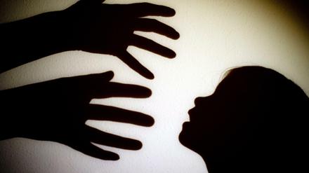 Schatten von Händen einer erwachsenen Person und dem Kopf eines Kindes sind an einer Wand eines Zimmers zu sehen. 