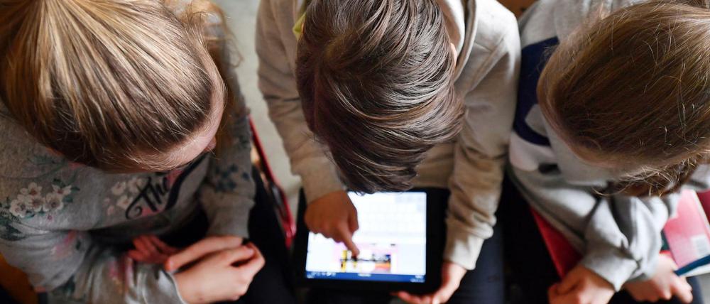 Drei Schüler beugen sich über einen Tablet-Computer.