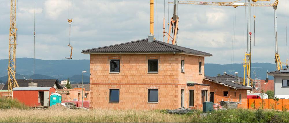Kräne in einer Neubausiedlung in Parkstetten (Bayern) hinter dem Rohbau von einem Einfamilienhaus.