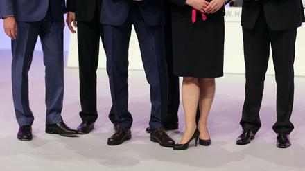 Mehrere männliche und ein weibliches Vorstandsmitglied stehen auf einer Hauptversammlung zusammen auf dem Podium. 