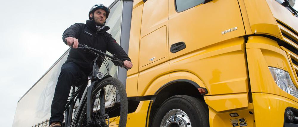 Ein Radfahrer steht mit seinem Fahrrad in der Versuchsabteilung von Mercedes Benz neben einem LKW mit einem Abbiegeassistenten.