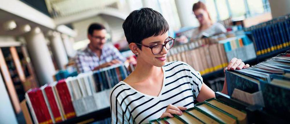 Studierende stehen in einer Unibibliothek an Bücherregalen.