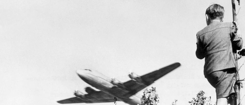 Ein Junge verfolgt von einem Baum aus den Landeanflug eines US-amerikanischen Transportflugzeugs auf den Berliner Flughafen Tempelhof.