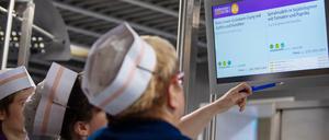 Drei Köchinnen schauen in der veganen Mensa auf dem Campus der Technischen Universität auf einen Monitor mit dem aktuellen Speiseplan. 