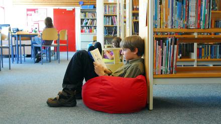 Kinder sitzen in einer Bibliothek auf Sitzsäcken und lesen.