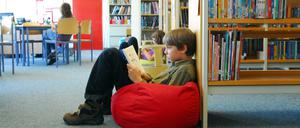 Kinder sitzen in einer Bibliothek auf Sitzsäcken und lesen.