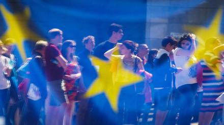 Menschen spiegeln sich in einem Fenster mit einer europäischen Flagge im Europäischen Parlament