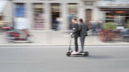 Zwei Personen fahren auf einem ausgeliehenen E-Scooter. 