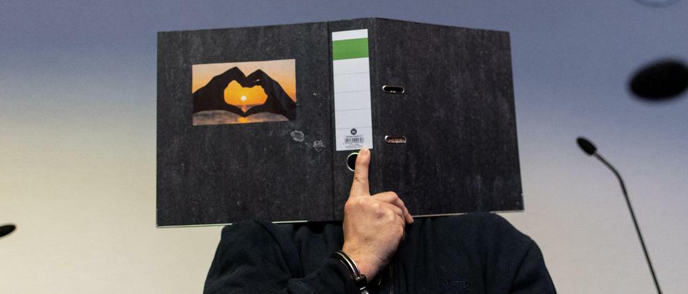 Der 58-jährige Angeklagte sitzt im Gerichtssaal und hält einen Aktenordner mit einem Herz aus zwei Händen vor sein Gesicht.