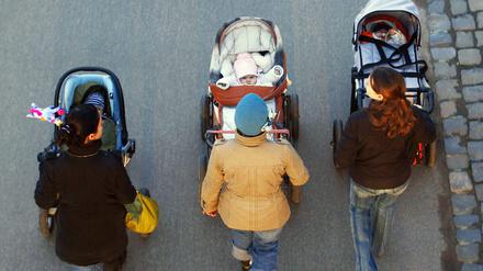 Drei junge Mütter schieben ihre Babys im Kinderwagen bei einem gemeinsamen Spaziergang. 