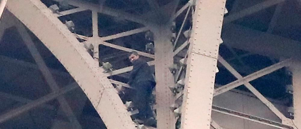 Ein Kletterer steht auf Eisenstreben hoch oben am Eifelturm.