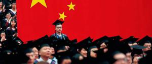 Hochschul-Absolventen in China feiern ihren Abschluss mit Doktorhüten auf dem Kopf - und vor einer überdimensionalen chinesischen Fahne.