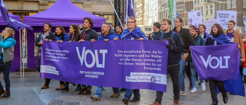 Mitglieder und Anhänger der proeuropäischen Partei Volt ziehen mit Flaggen und Bannern in Amsterdam durch eine Straße.