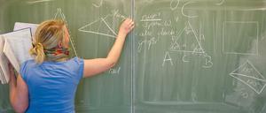  Eine Lehrerin schreibt mit Kreide an die Tafel. 