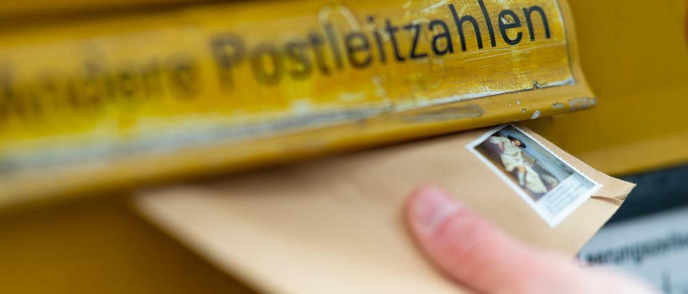 Ein Mann wirft einen Brief in einen Briefkasten. Das Briefporto soll zum 1. Juli steigen.