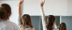 Oberstufenschülerinnen sitzen in einem Klassenraum und melden sich im Unterricht.