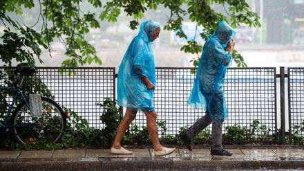 06.06.2019, Berlin: Eine Frau und ein Mann laufen in blauen Regencapes durch den Regen. Foto: Lisa Ducret/dpa +++ dpa-Bildfunk +++