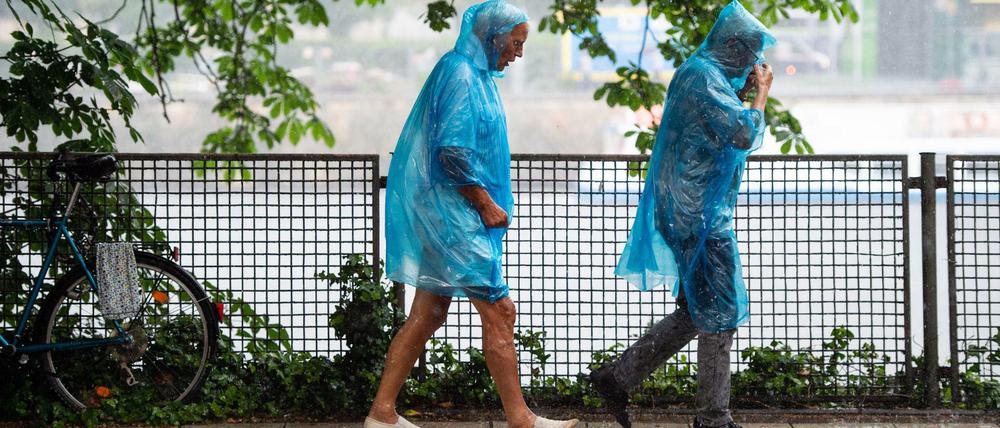 06.06.2019, Berlin: Eine Frau und ein Mann laufen in blauen Regencapes durch den Regen. Foto: Lisa Ducret/dpa +++ dpa-Bildfunk +++