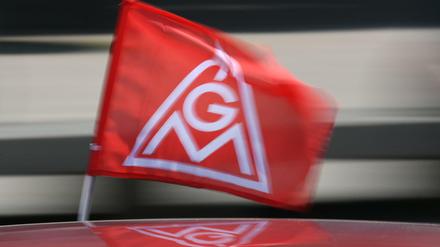 Eine IG-Metall-Flagge spiegelt sich in einem Fahrzeugdach. Die größte deutsche Gewerkschaft ist am stärksten in der Autoindustrie - und hier steht ein tiefer Wandel bevor. 