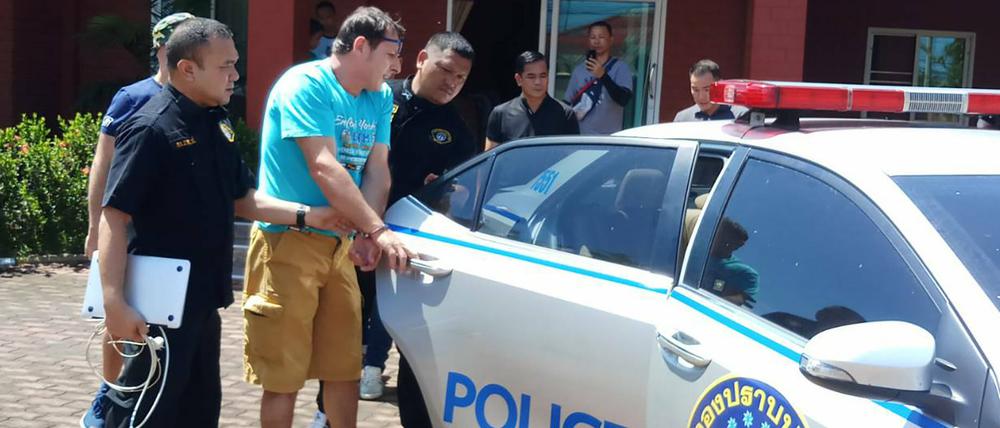 Francesco G. aus Italien, der von thailändischen Polizisten zu einem Polizeiauto geführt wird.