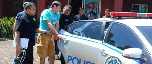 Francesco G. aus Italien, der von thailändischen Polizisten zu einem Polizeiauto geführt wird.