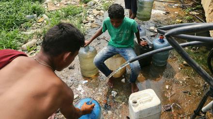 Menschen sammeln Trinkwasser aus defekten Leitungen in der Nähe einer Barackensiedlung in Venezuela.