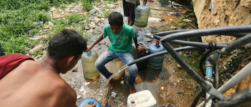 Menschen sammeln Trinkwasser aus defekten Leitungen in der Nähe einer Barackensiedlung in Venezuela.