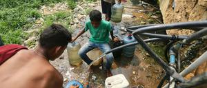 Menschen sammeln Trinkwasser aus defekten Leitungen in der Nähe einer Barackensiedlung in Venezuela.