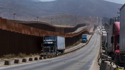 Lastwagen fahren in Tijuana an einem Grenzzaun vorbei, bevor sie über die Grenze in die USA fahren.
