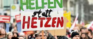 Ein Teilnehmer einer Demonstration hält ein Plakat mit der Aufschrift "Helfen statt Hetzen" in die Höhe (Symbolfoto).