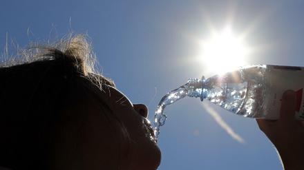 Bei Temperaturen um 33 Grad Celsius erfrischt sich eine junge Frau in Berlin-Spandau mit sprudelndem Mineralwasser. 