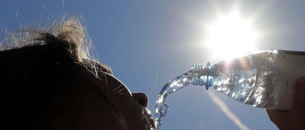 Bei Temperaturen um 33 Grad Celsius erfrischt sich eine junge Frau in Berlin-Spandau mit sprudelndem Mineralwasser.